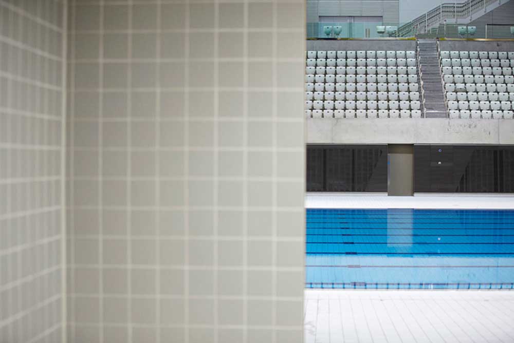 looking out from changing room to swimming pool with empty seats at aquatic centre by airey spaces