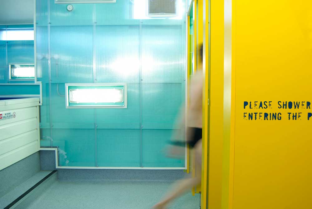 man entering yellow shower cubicle in swimming pool centre by airey spaces